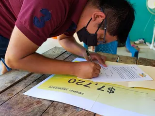Raúl firmando la entrega de lo reunido en una campaña de Help Land, junto al cheque simbólico de 7,720 pesos