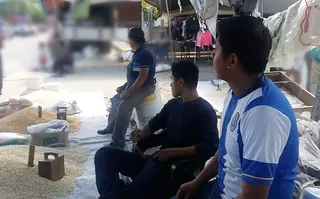 Raúl con su papá y un amigo en su puesto de maíz del tianguis de Platón Sánchez, con el maíz sobre la lona y las pesas de fierro